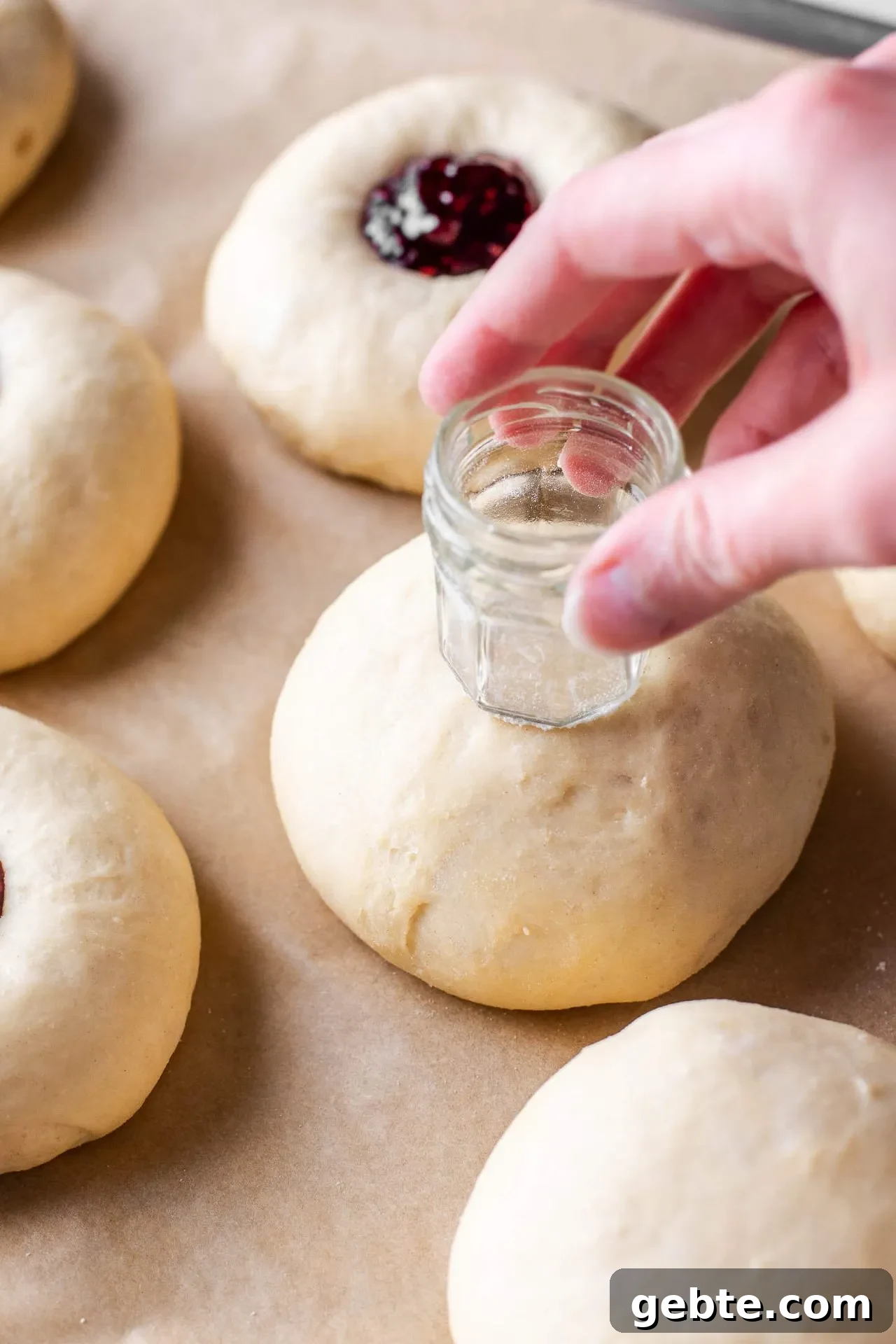 baked raspberry donuts dough balls on parchment lined baking sheet with jar pushing center indent in buns