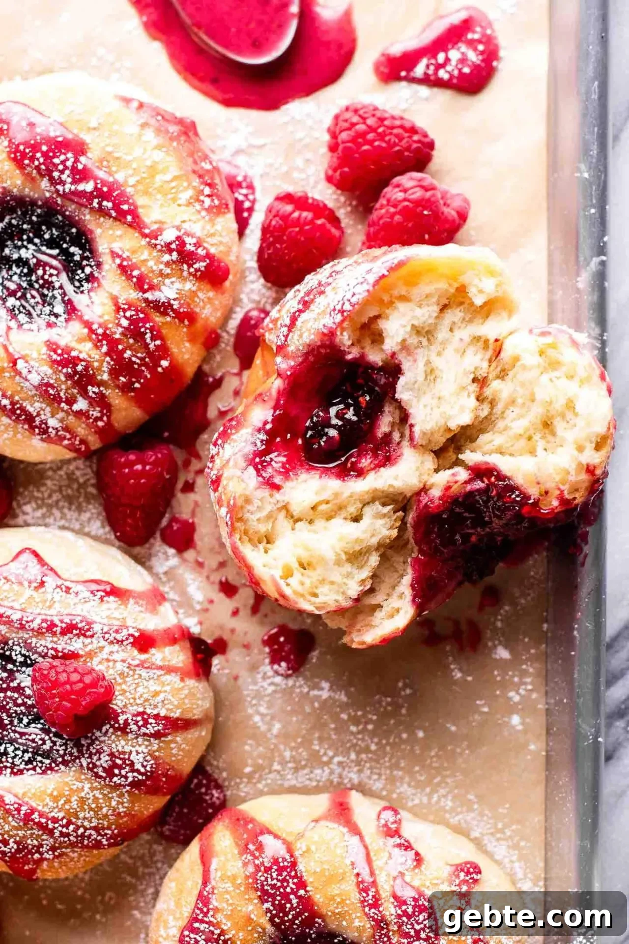 baked raspberry donuts on parchment lined baking sheet topped with icing and a light dusting of powdered sugar