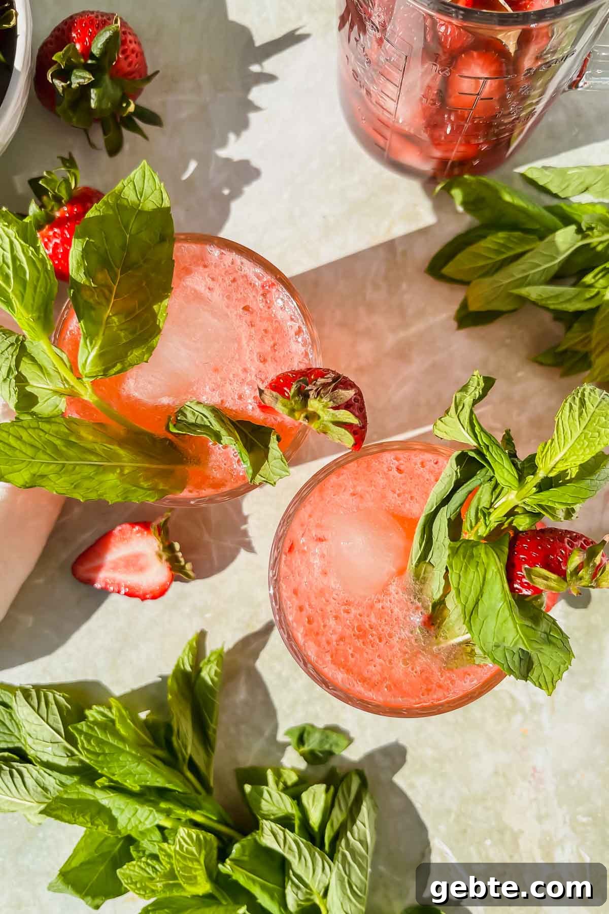 Strawberry Gin Smash: Refreshing Cocktail Recipe for Summer 8 overhead view of two strawberry gin smash cocktails garnished with mint and fresh strawberry slices.