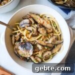 white bowl with spaghetti and mushrooms topped with red pepper flake and fresh thyme