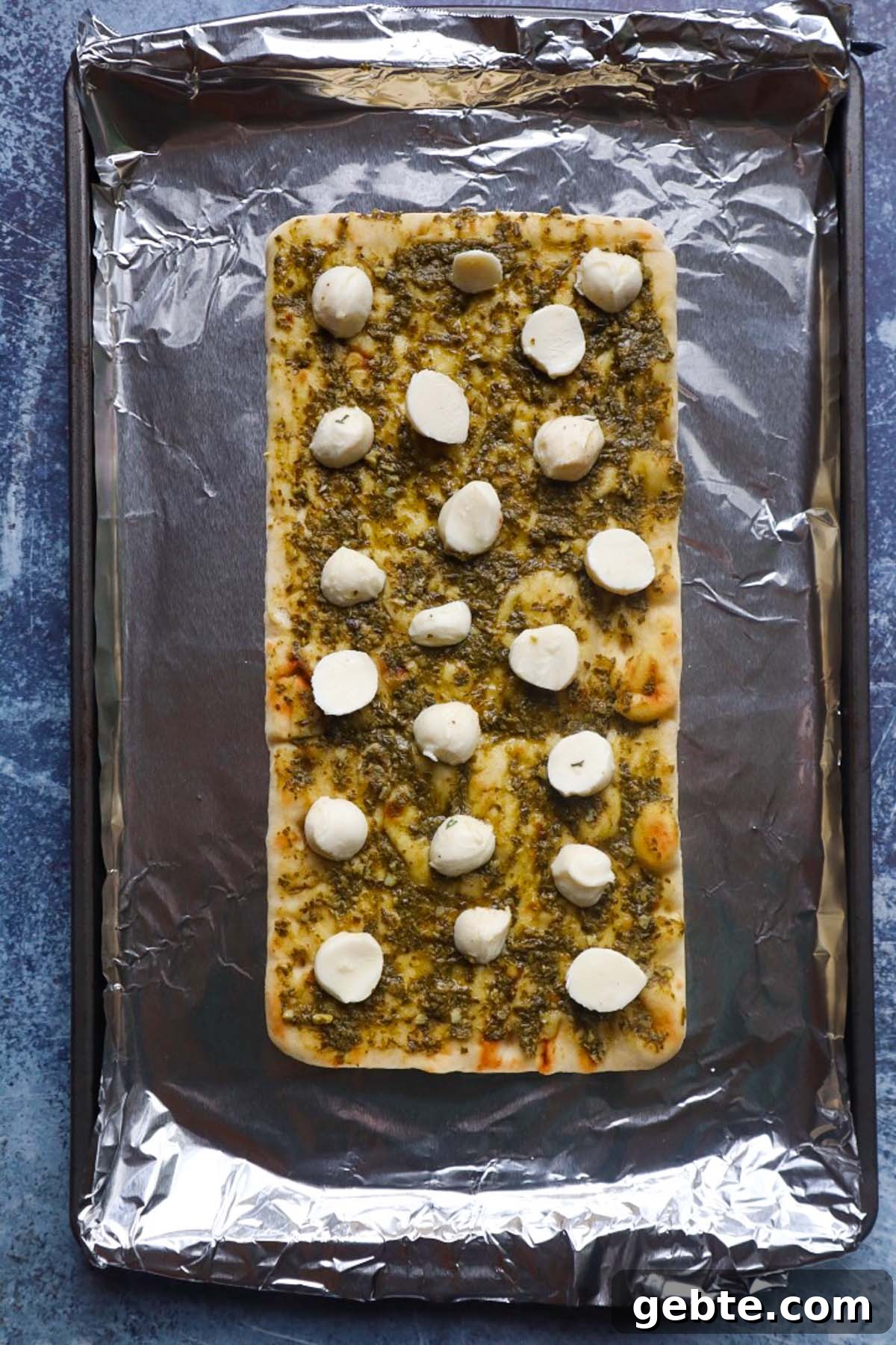 baking pan covered in foil with flatbread topped with pesto and mozzarella