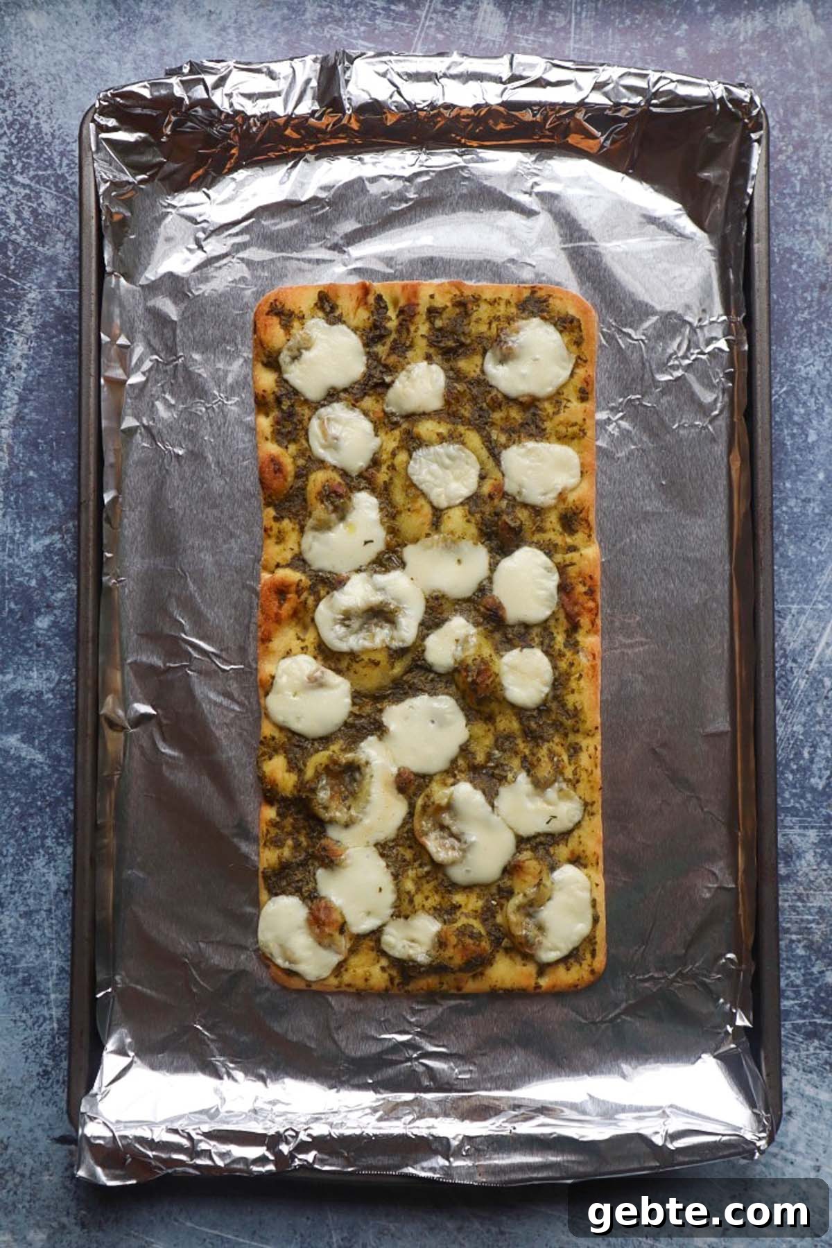 baking pan covered in foil with flatbread topped with pesto and mozzarella