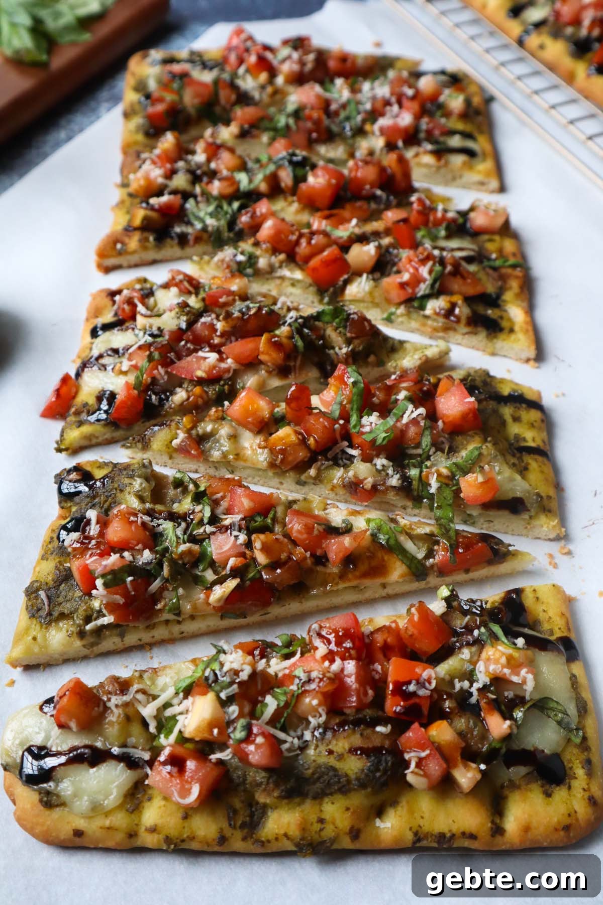parchment paper with flatbread topped with bruschetta, cheese, and balsamic glaze