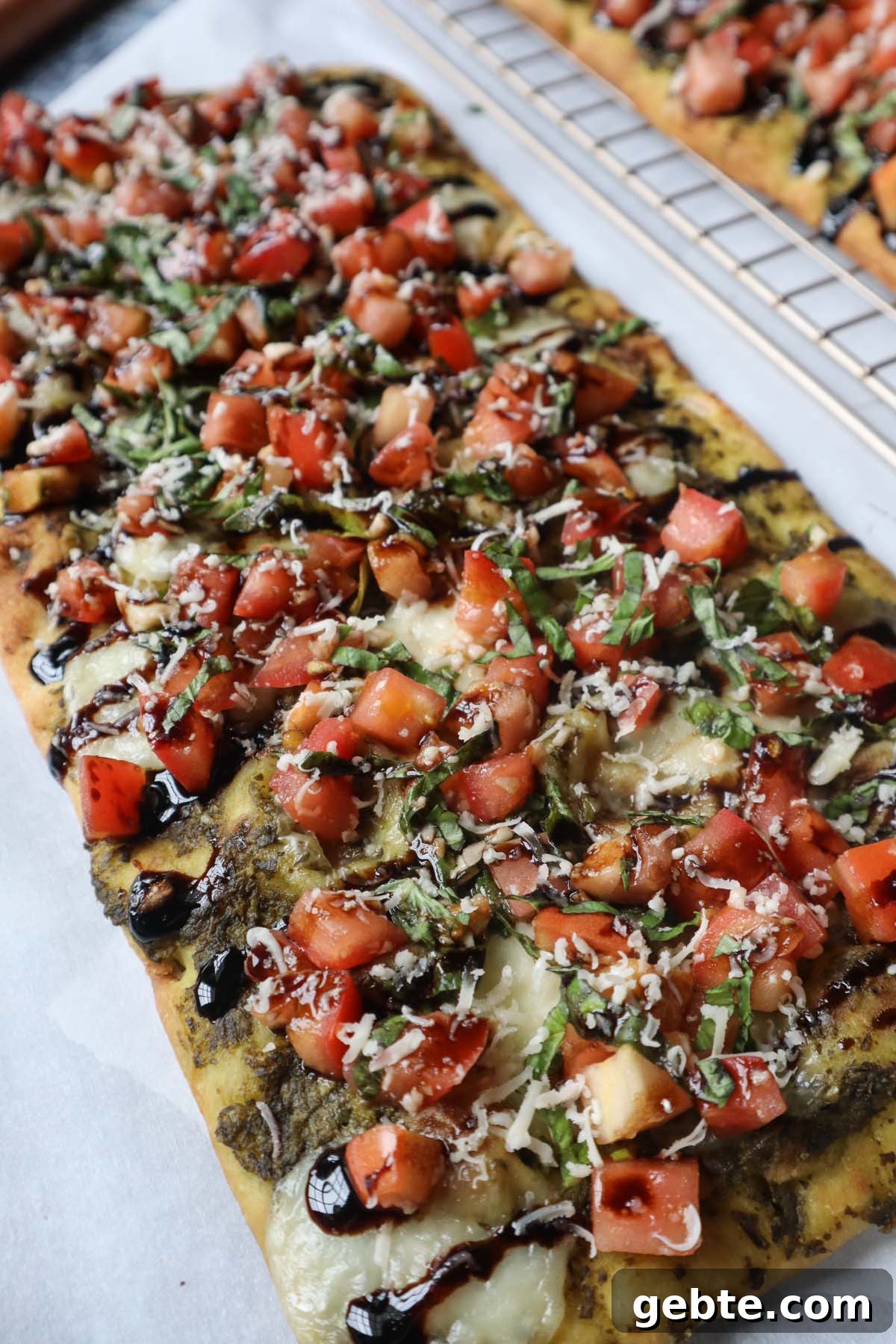parchment paper with flatbread topped with bruschetta, cheese, and balsamic glaze