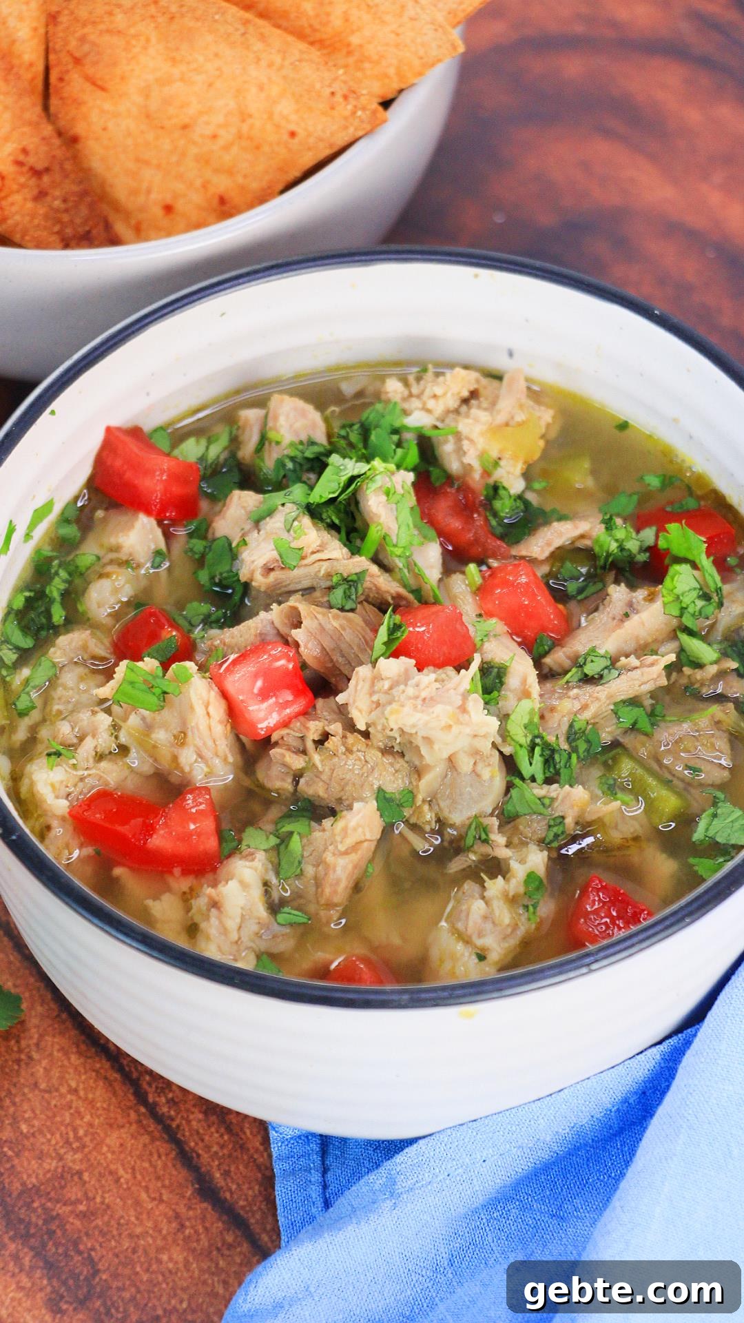 Savory Pulled Pork Green Chile (Chili Verde) Recipe 11 Sideview of a bowl of green chili pork soup garnished with Cilantro and chopped tomatoes - Hostess At Heart