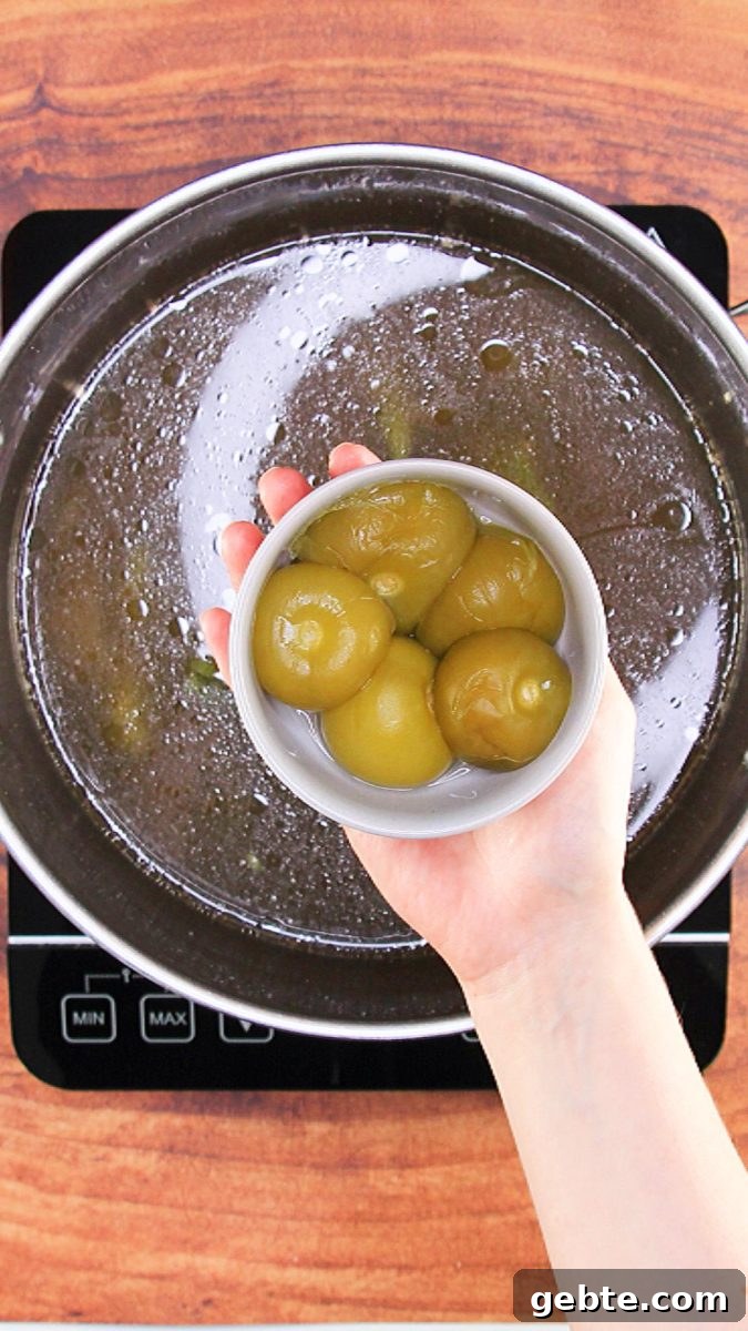 Savory Pulled Pork Green Chile (Chili Verde) Recipe 5 A bowl filled with 5 tomatillos hovering over a cooking pot - Hostess At Heart