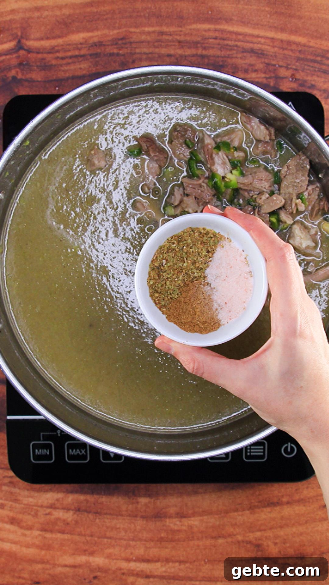 Savory Pulled Pork Green Chile (Chili Verde) Recipe 8 A pot filled with green verde and pulled pork with a dish of spices being added - Hostess At Heart