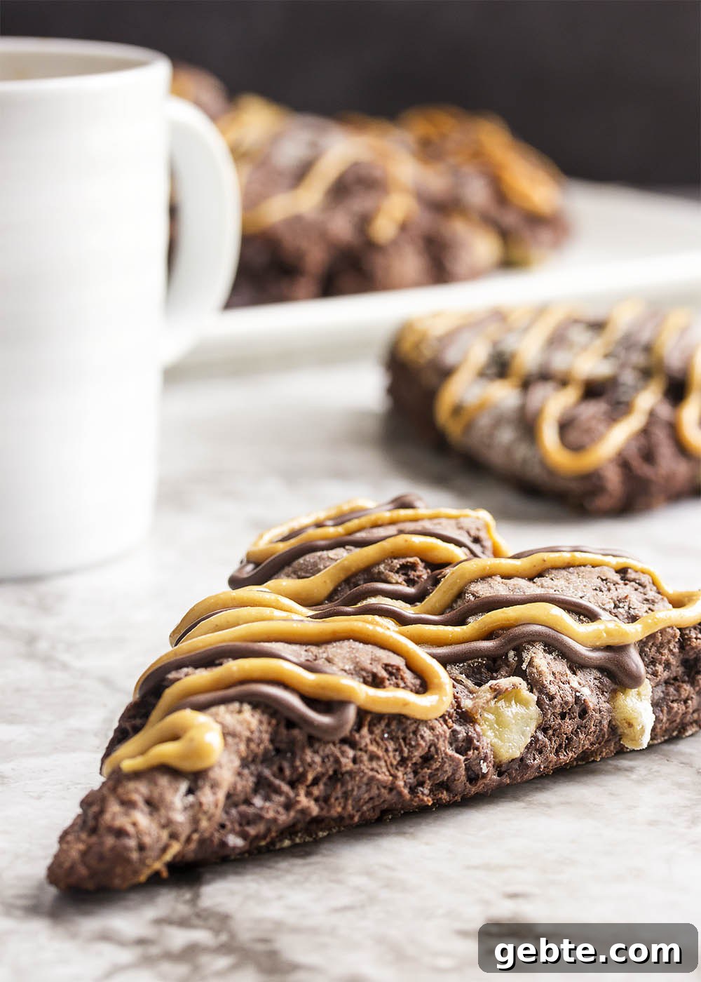 Triple Chocolate Banana Scones - These triple chocolate scones are studded with banana chunks in an intensely chocolatey batter and then topped with chocolate glaze and a peanut butter drizzle. Have them for breakfast or dessert and they would be perfect for a brunch.