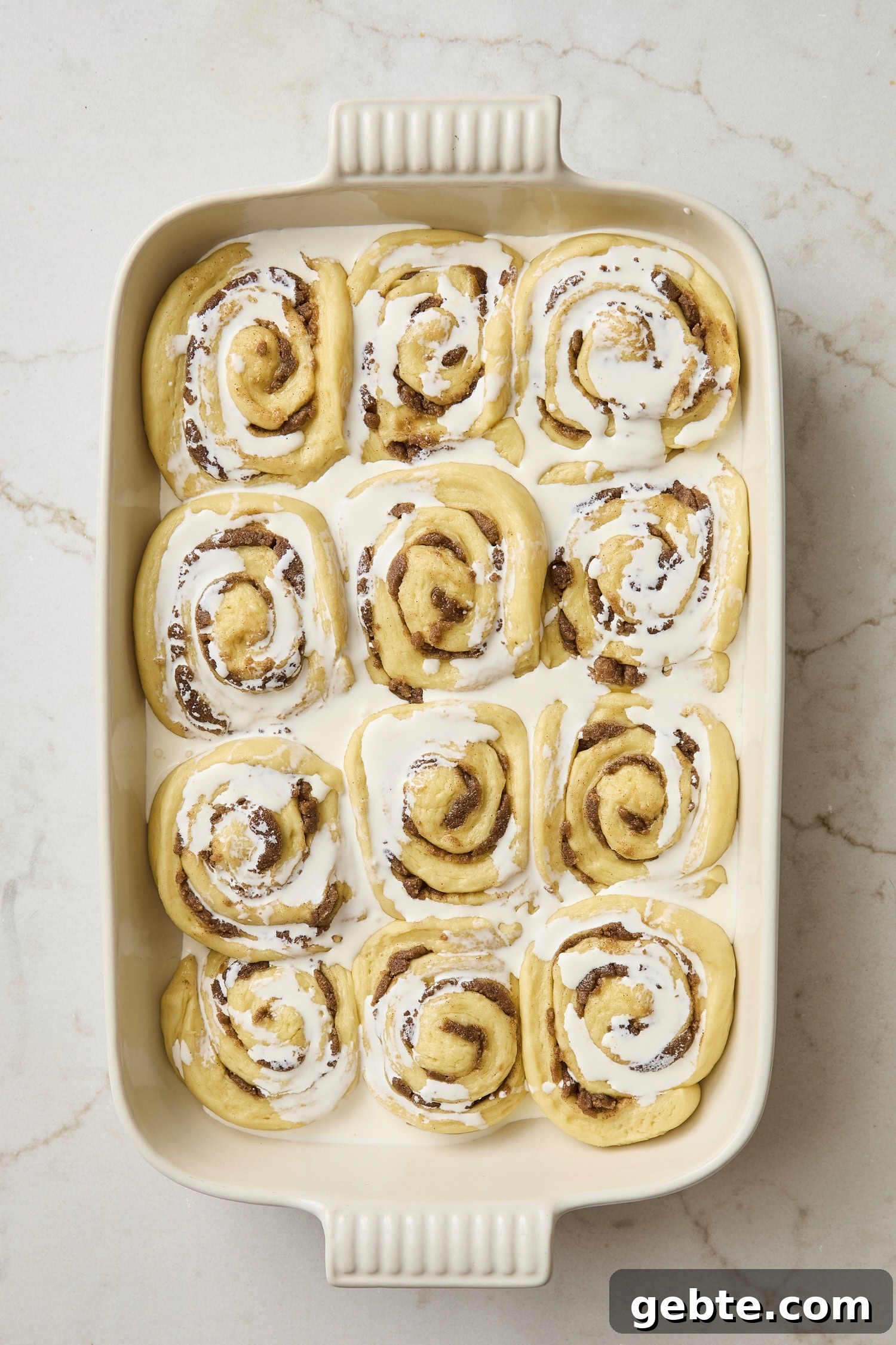 Unbaked cinnamon rolls with heavy cream poured on top before going into the oven.