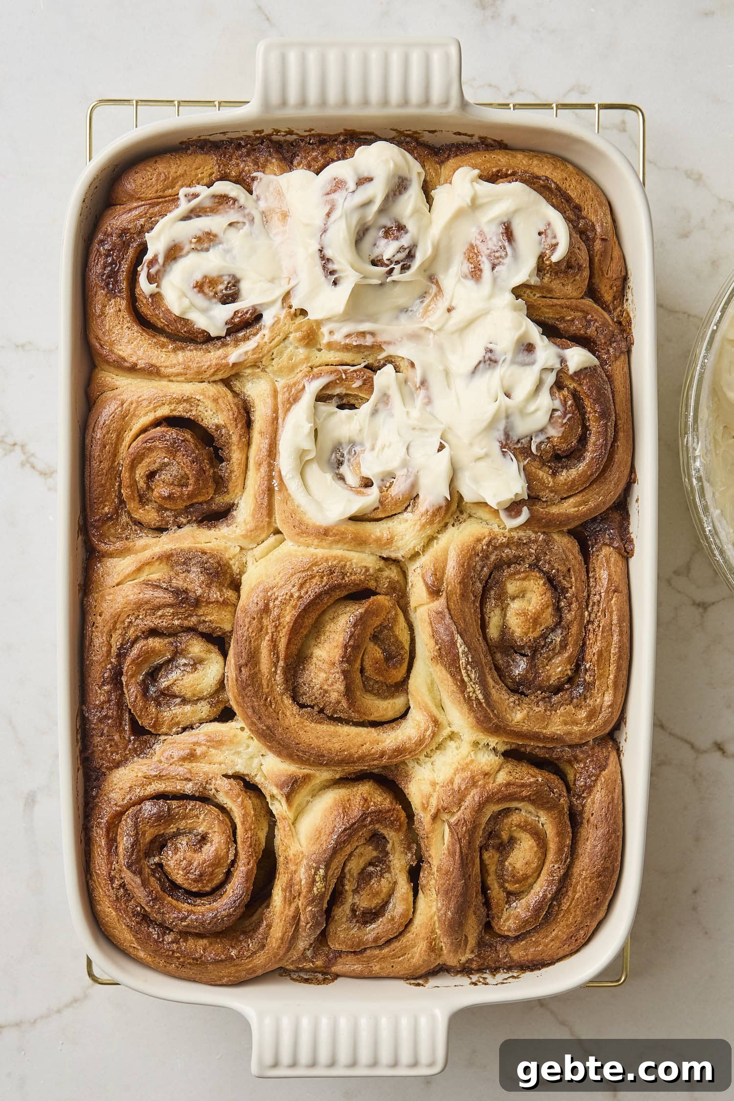 Baked cinnamon rolls partially frosted with cream cheese frosting.