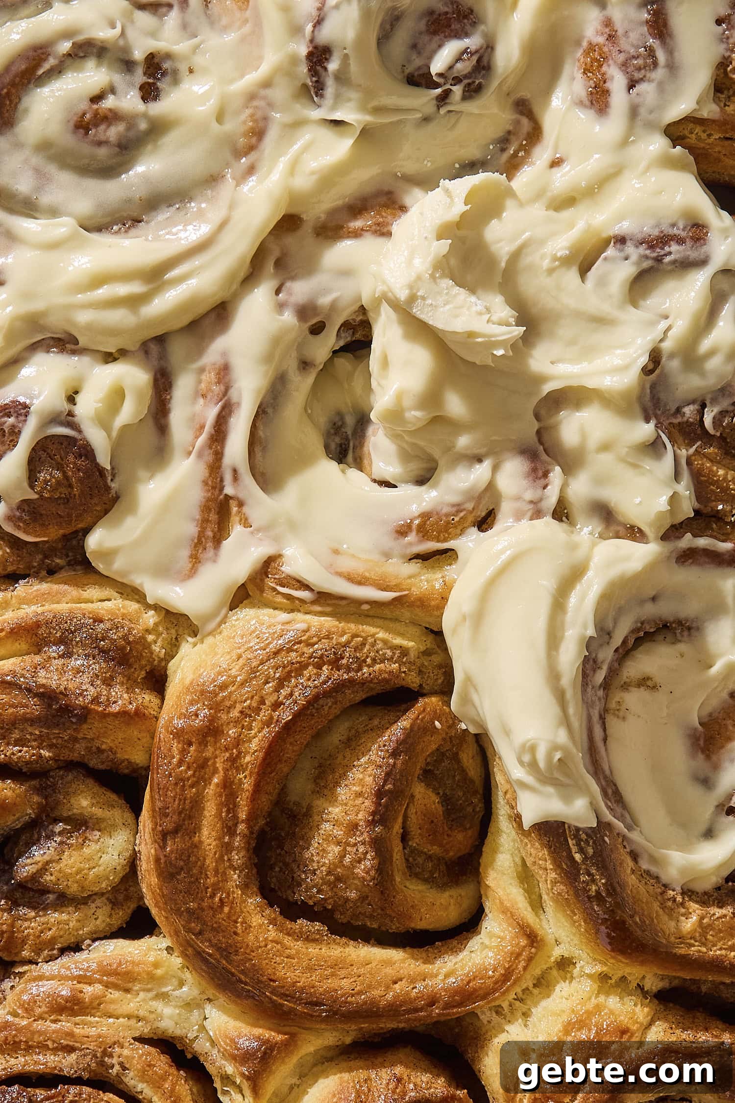 Baked brioche cinnamon rolls with cream cheese frosting partially covering rolls.