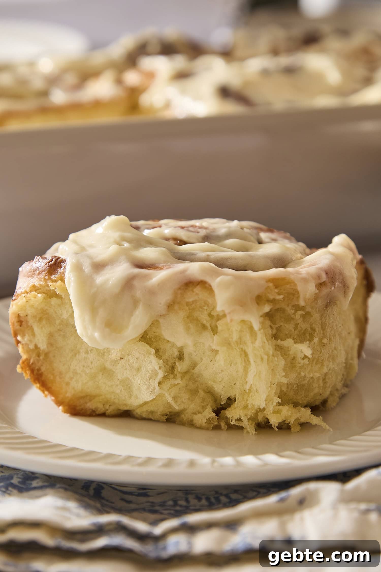 Plate with single cinnamon roll topped with cream cheese frosting.