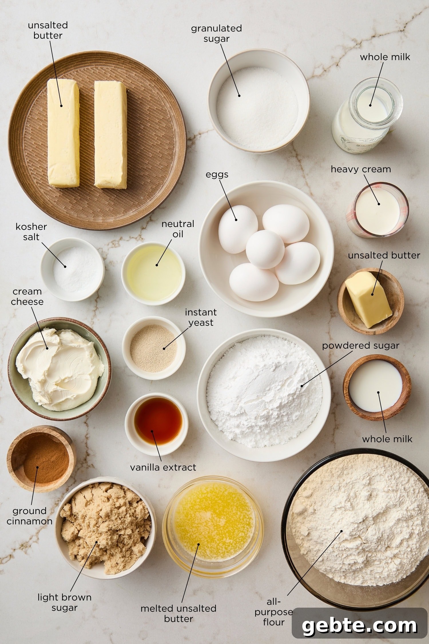 Countertop surface with ingredients needed for cinnamon rolls including butter, flour, sugar, and more.
