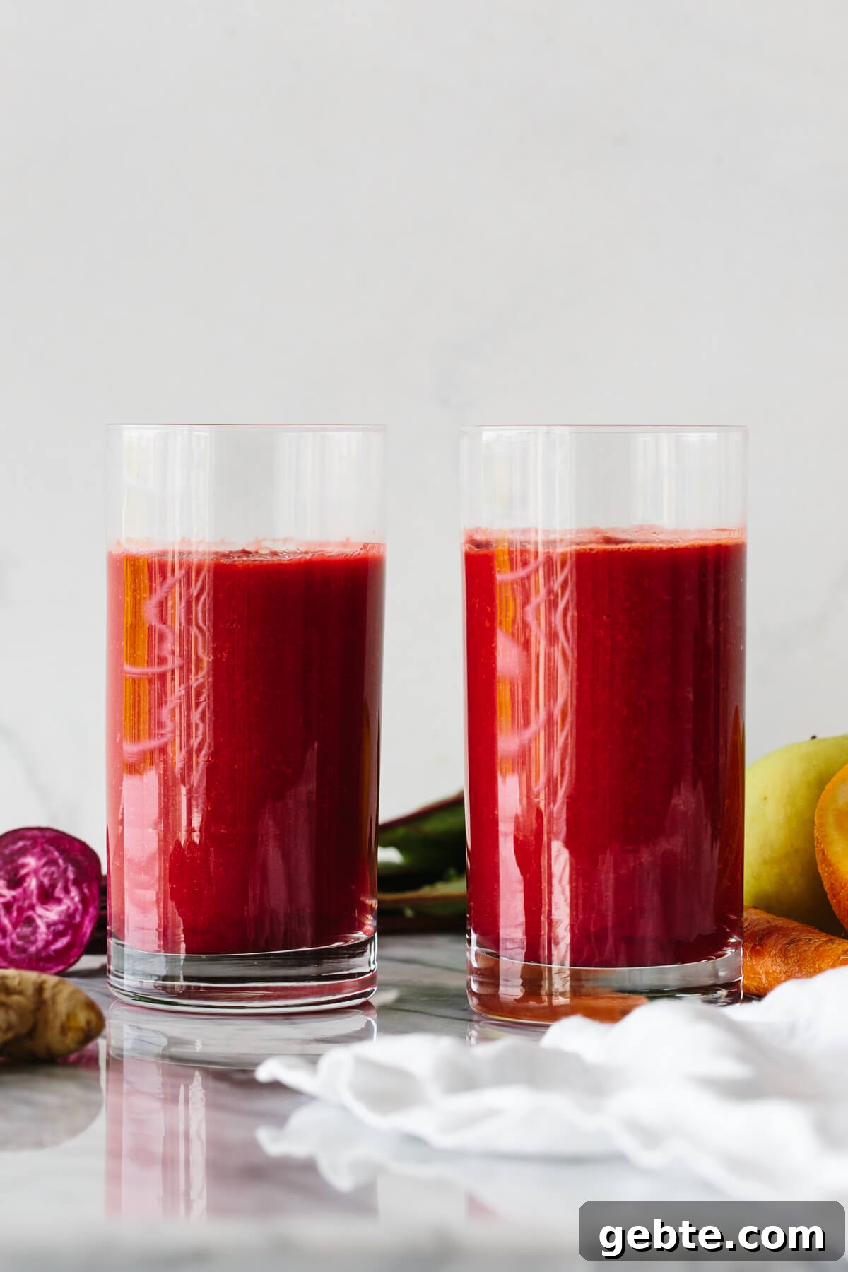 Top Anti-Inflammatory Drinks to Boost Immunity and Reduce Inflammation 11 Two glasses of apple, carrot, beet smoothie surrounded by fresh produce.