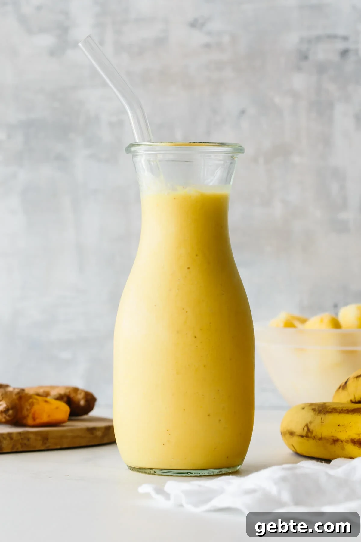 Top Anti-Inflammatory Drinks to Boost Immunity and Reduce Inflammation 7 Turmeric smoothie in a glass jar with straw and ingredients in the background.