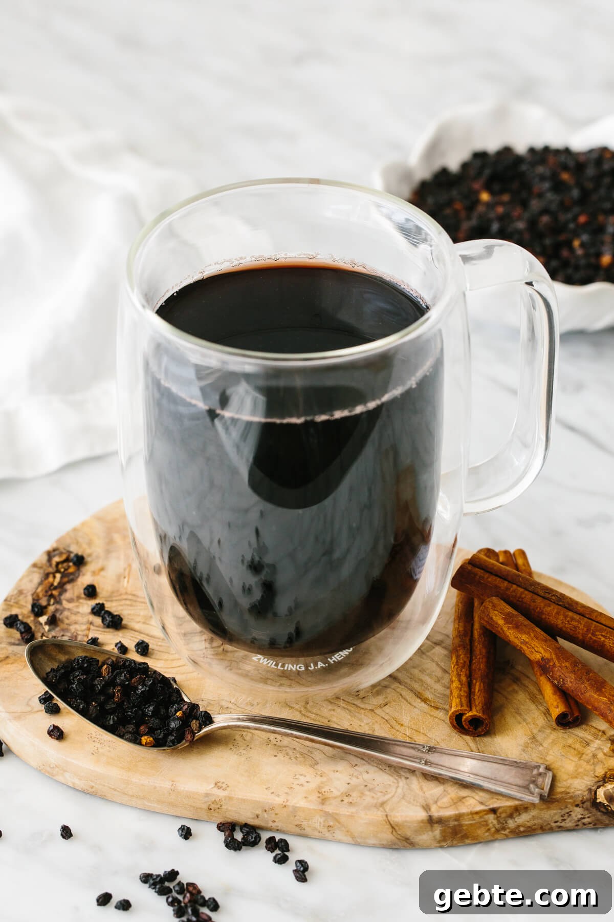 Top Anti-Inflammatory Drinks to Boost Immunity and Reduce Inflammation 10 Elderberry tea in a glass next to dried elderberry and cinnamon sticks.
