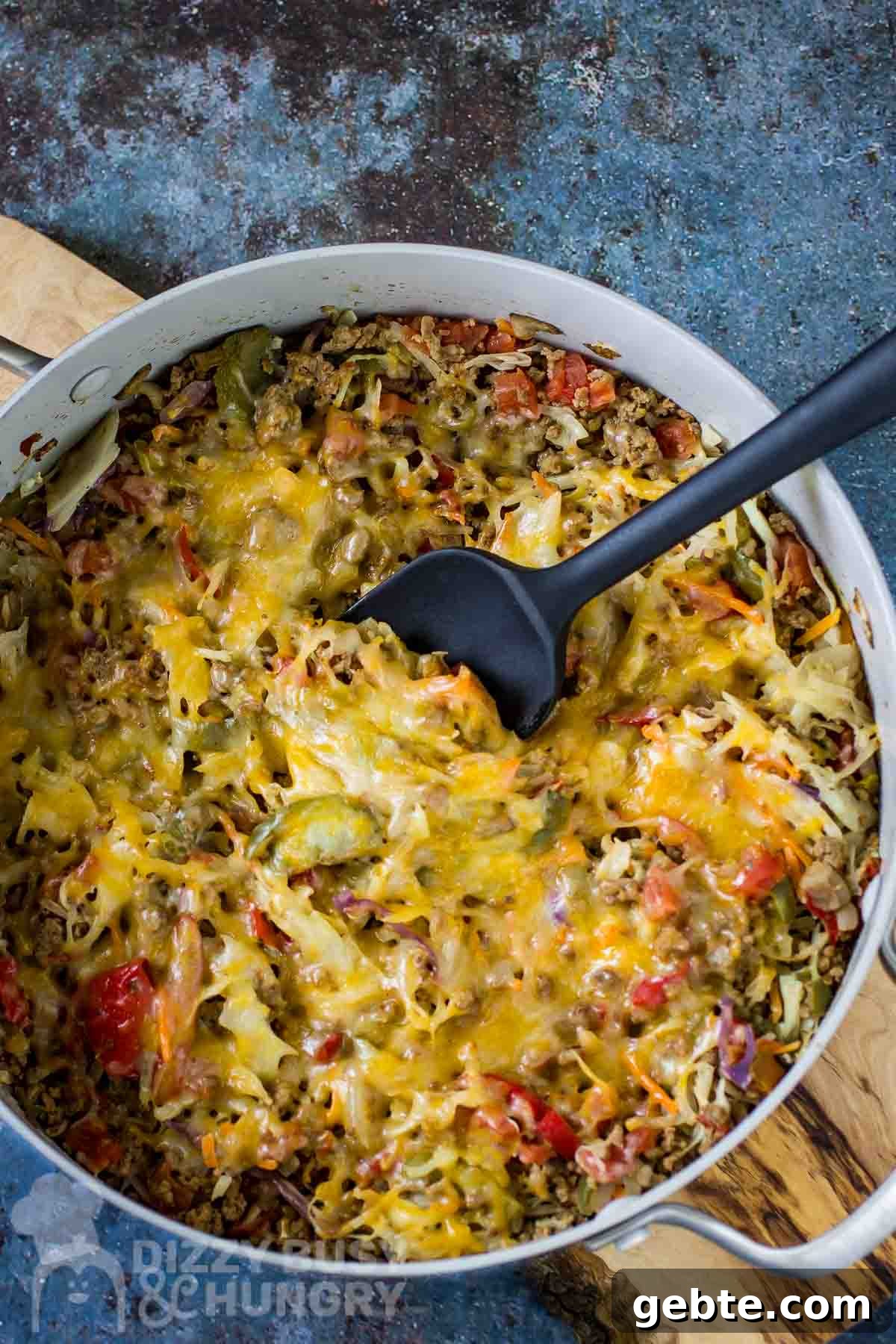 One-Skillet Stuffed Cabbage Casserole Recipe for Quick Weeknights 2 Overhead shot of cabbage casserole in a large shallow pot with a black spatula all resting on a wooden surface.