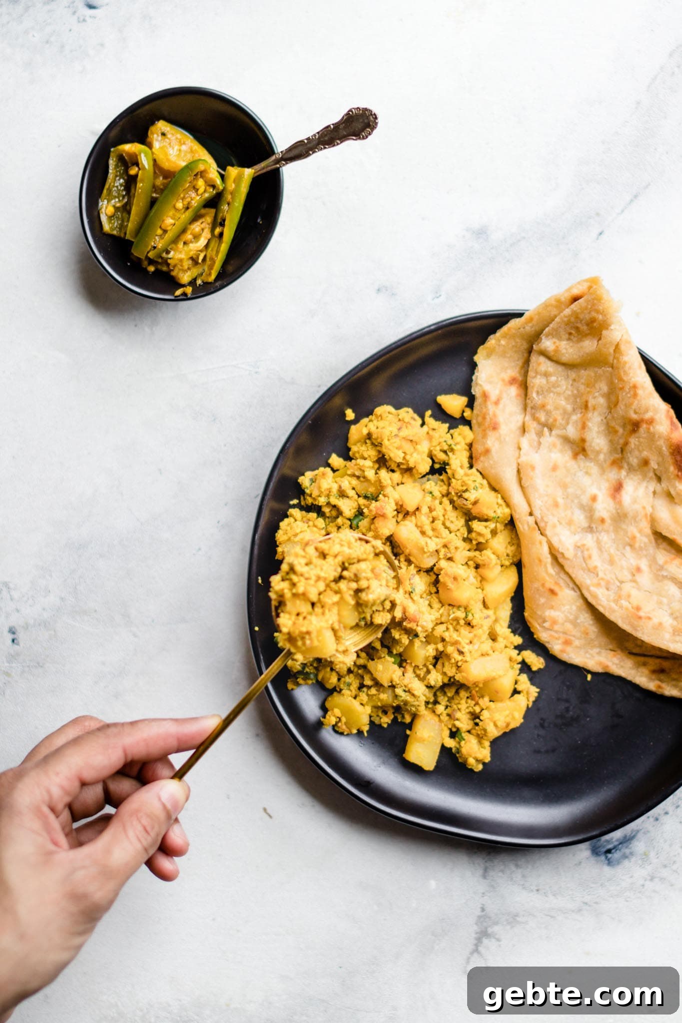 Holding a spoon with scrambled egg and potato curry over a plate