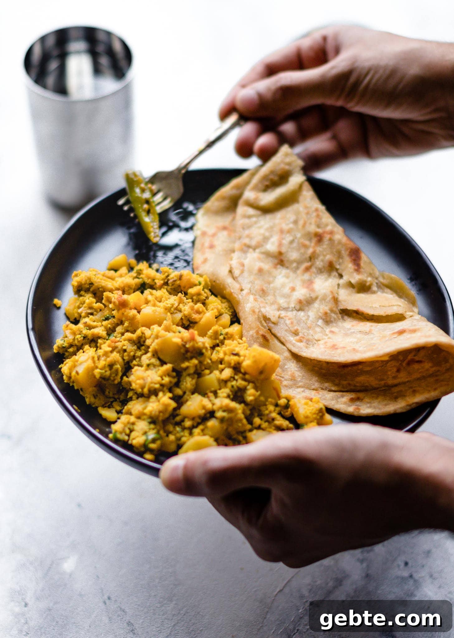 Holding a fork and a plate of scrambled egg and potatoes with paratha