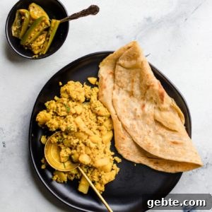 Scrambled Egg and Potatoes and paratha on a black plate with a gold spoon