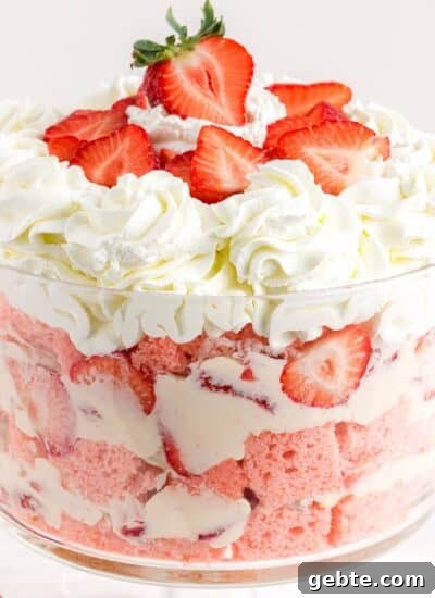 Strawberry cheesecake trifle presented as layers of strawberry cake, whipped cream, and fresh strawberries in a glass trifle dish.