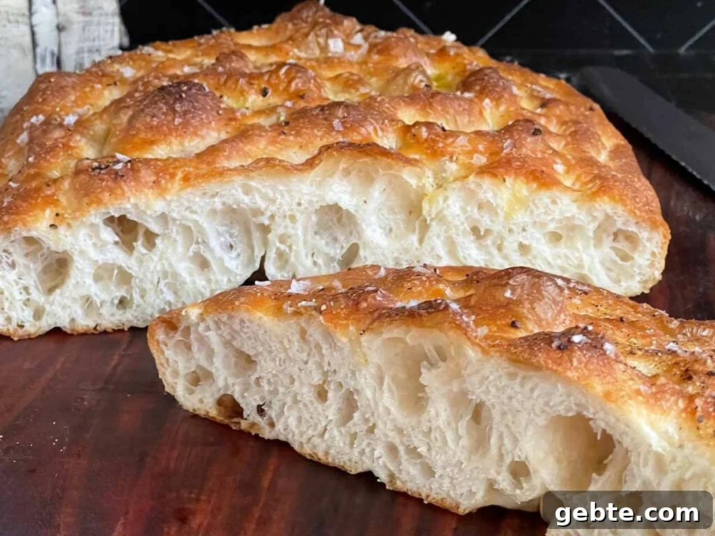 Overnight focaccia bread cut in half on a wooden cutting board.