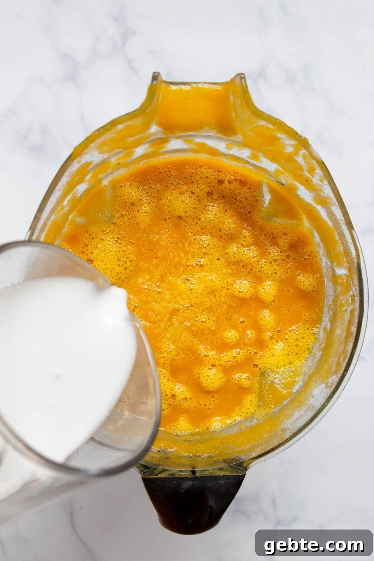 Creamy Carrot & Butternut Squash Soup Recipe for Fall Nights 11 Pouring coconut milk into blended butternut squash and carrot soup to make it creamy and dairy-free.