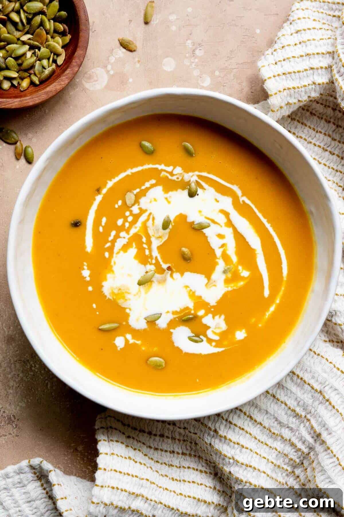 Creamy Carrot & Butternut Squash Soup Recipe for Fall Nights 12 Creamy carrot and butternut squash soup served in a bowl, topped with a swirl of coconut milk and crunchy pumpkin seeds.