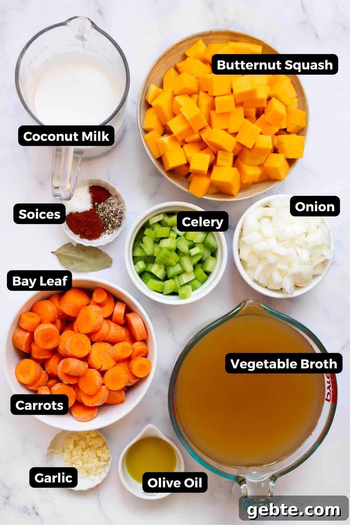 Creamy Carrot & Butternut Squash Soup Recipe for Fall Nights 3 All the ingredients for carrot and butternut squash soup arranged in small labeled bowls, including cubed butternut squash, sliced carrots, onion, celery, garlic, coconut milk, vegetable broth, olive oil, and spices.