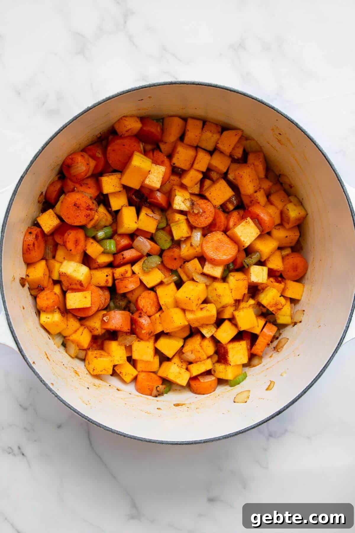 Creamy Carrot & Butternut Squash Soup Recipe for Fall Nights 7 Cubed butternut squash and spices being added to a pot with sautéed vegetables.