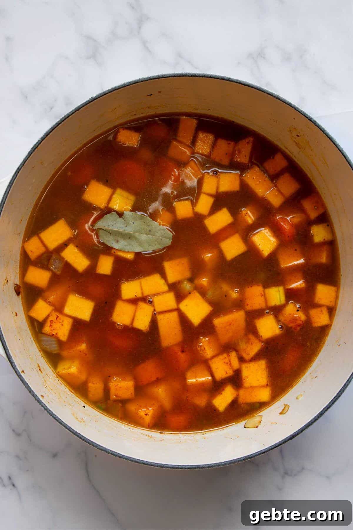 Creamy Carrot & Butternut Squash Soup Recipe for Fall Nights 8 Bay leaf and vegetable broth being poured into a pot with butternut squash, carrots, and aromatics.