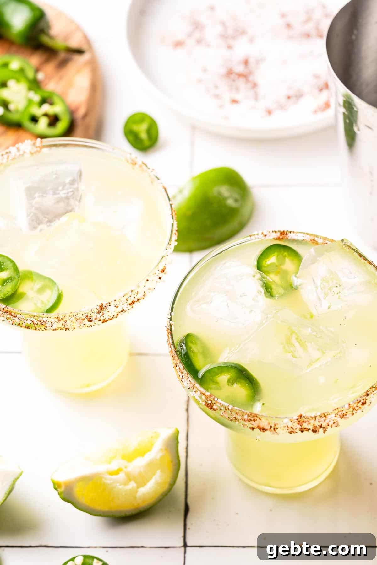 spicy margaritas in 2 glasses with jalapeño and salt in the background