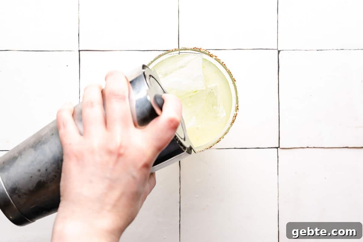 pouring margarita from cocktail shaker into glass