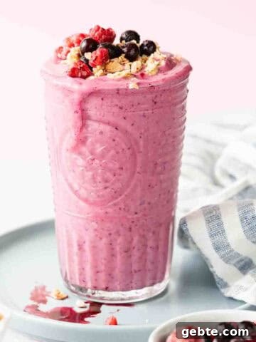 glass filled with berry smoothie topped with berries and granola.