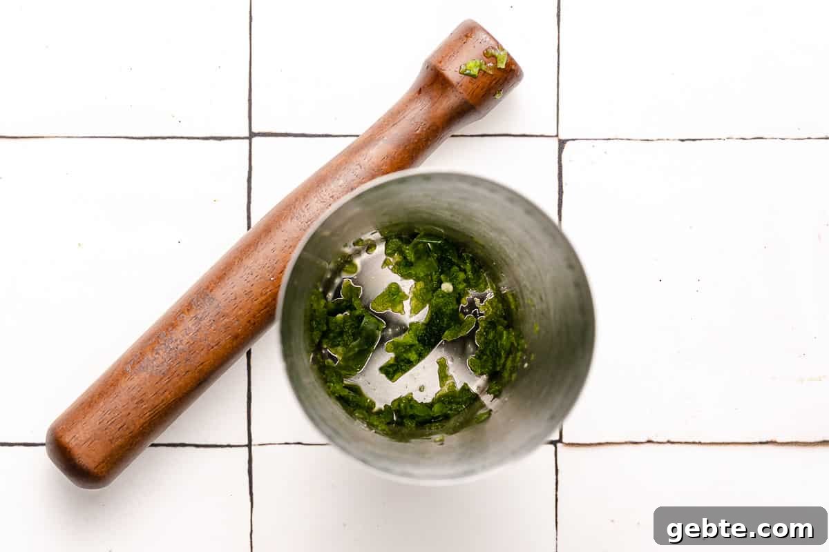 muddled pepper at the bottom of a cocktail shaker with muddler on the side