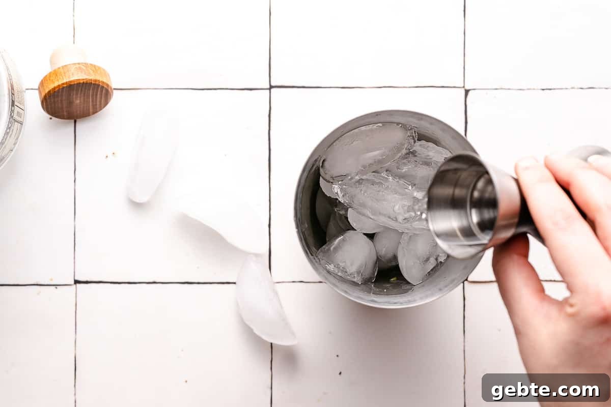 tequila being poured in a cocktail shaker filled with ice