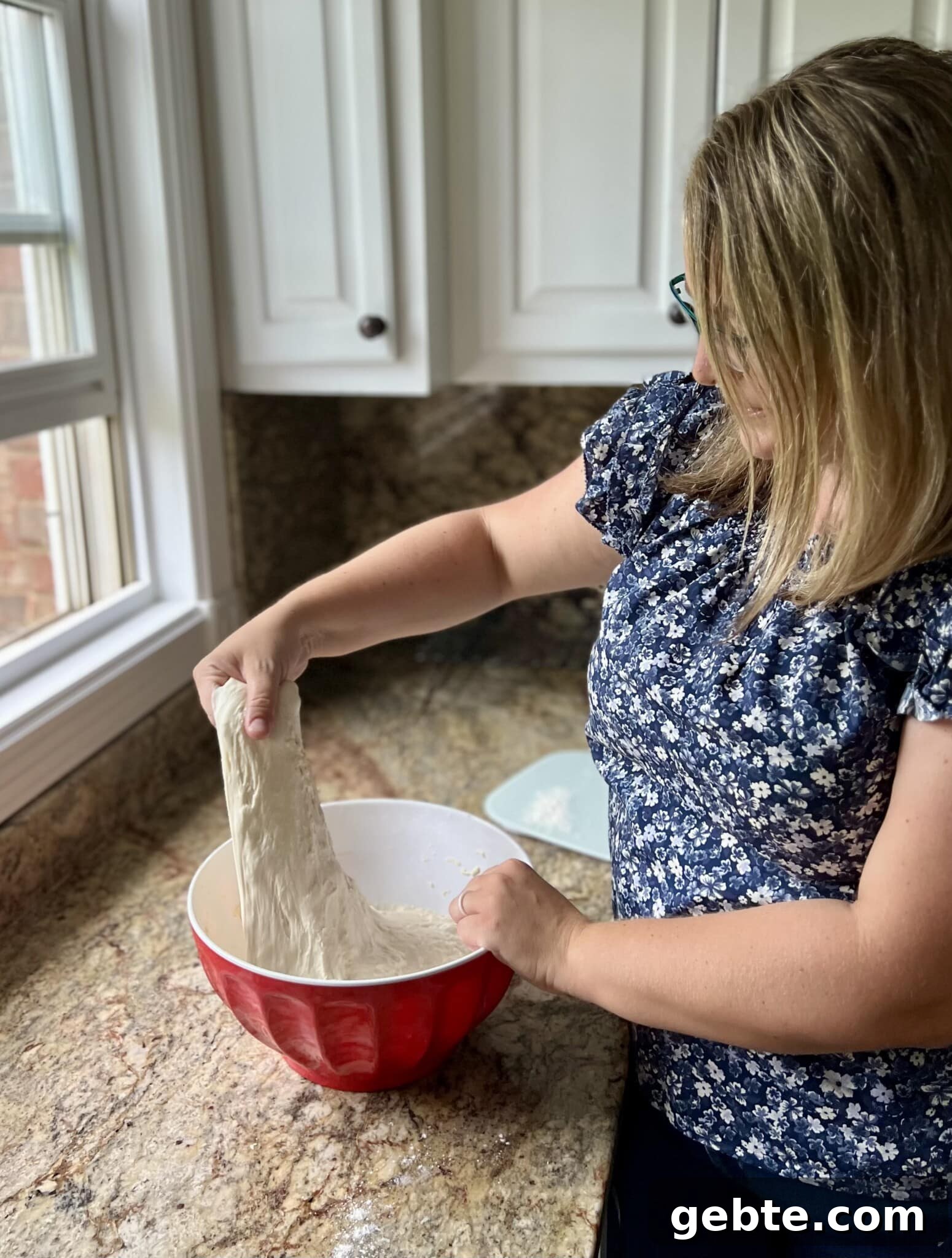 Sourdough Schedule for Beginners: Fit Baking into Your Daily Routine 9 Amy Coyne stretching sourdough bread in a bowl on a counter.
