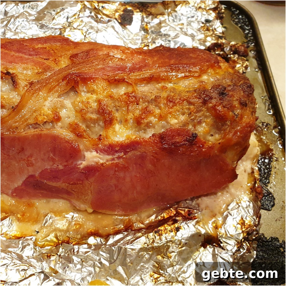 Bacon-Wrapped Meatloaf with Homemade Tomato Sauce 3 A cooked bacon covered meatloaf on tinfoil.