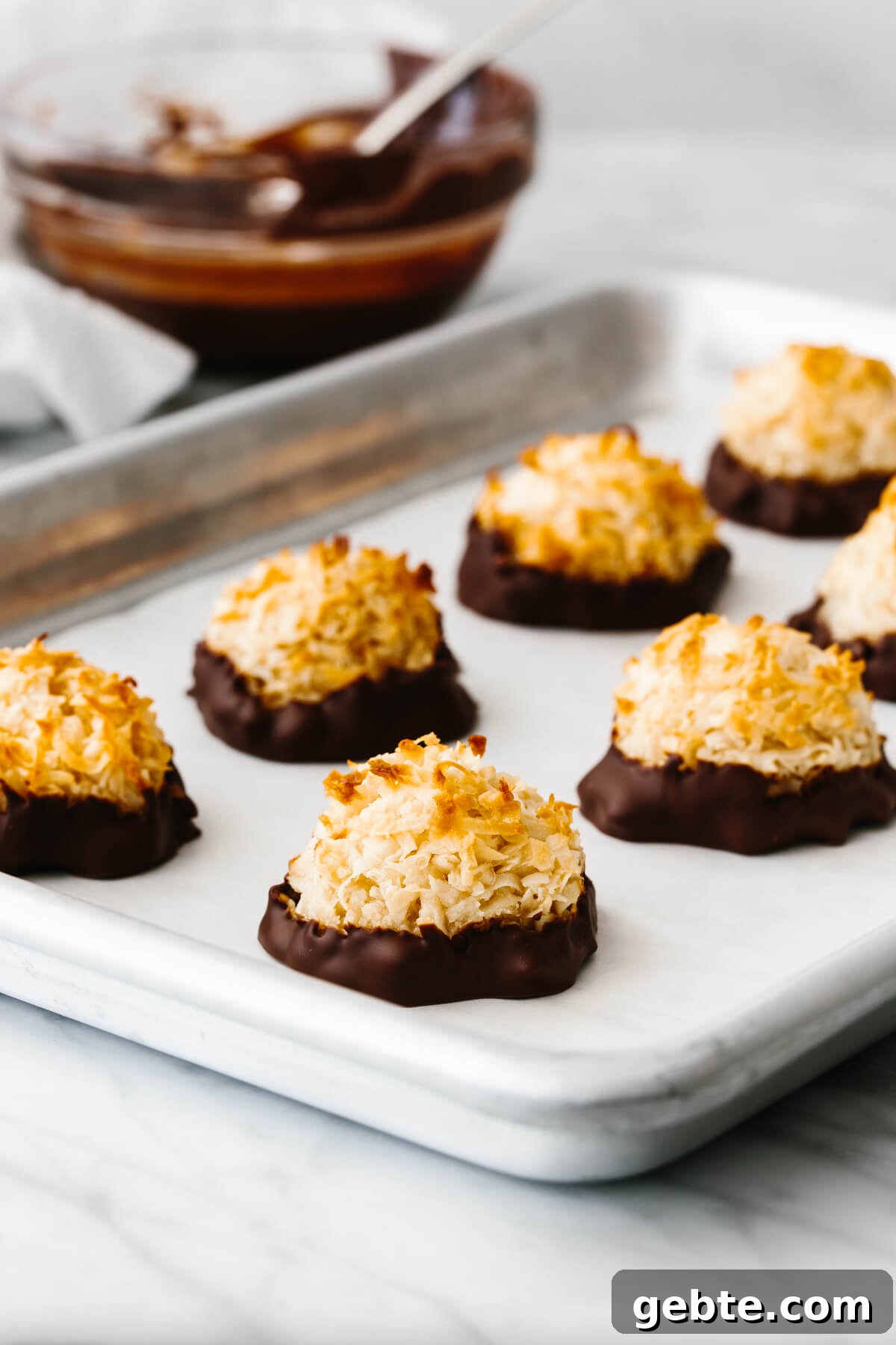 Coconut macaroons on a baking sheet next to a bowl of chocolate.