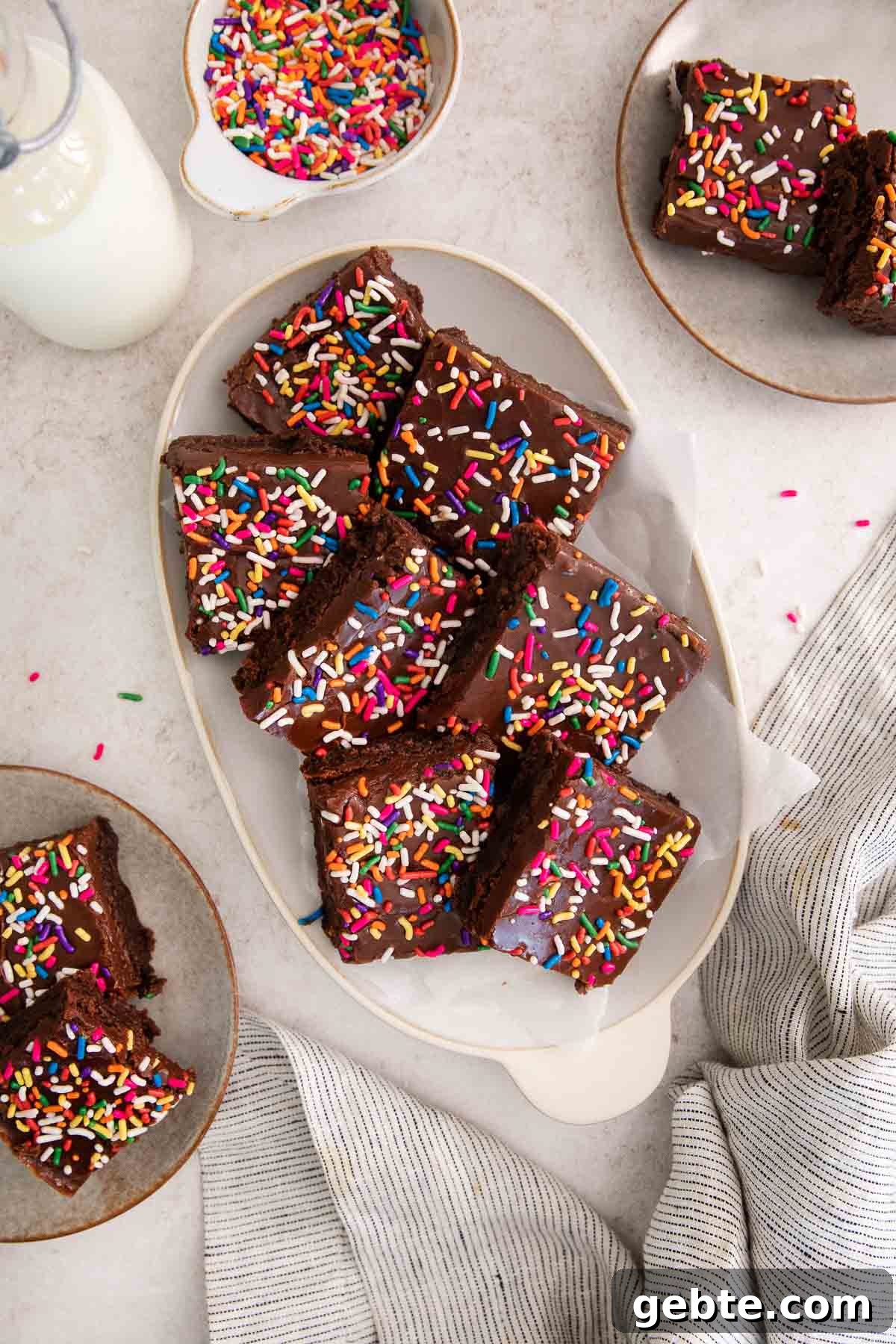 sliced brownies topped with fudge frosting and rainbow sprinkles on a platter.