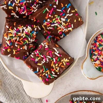 fudge-frosted brownies topped with sprinkles on a platter.