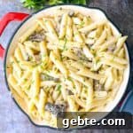 A beautifully presented skillet of Morel Mushroom Pasta, with a wooden spoon ready to serve the dish, and a sprinkle of fresh parsley on top.