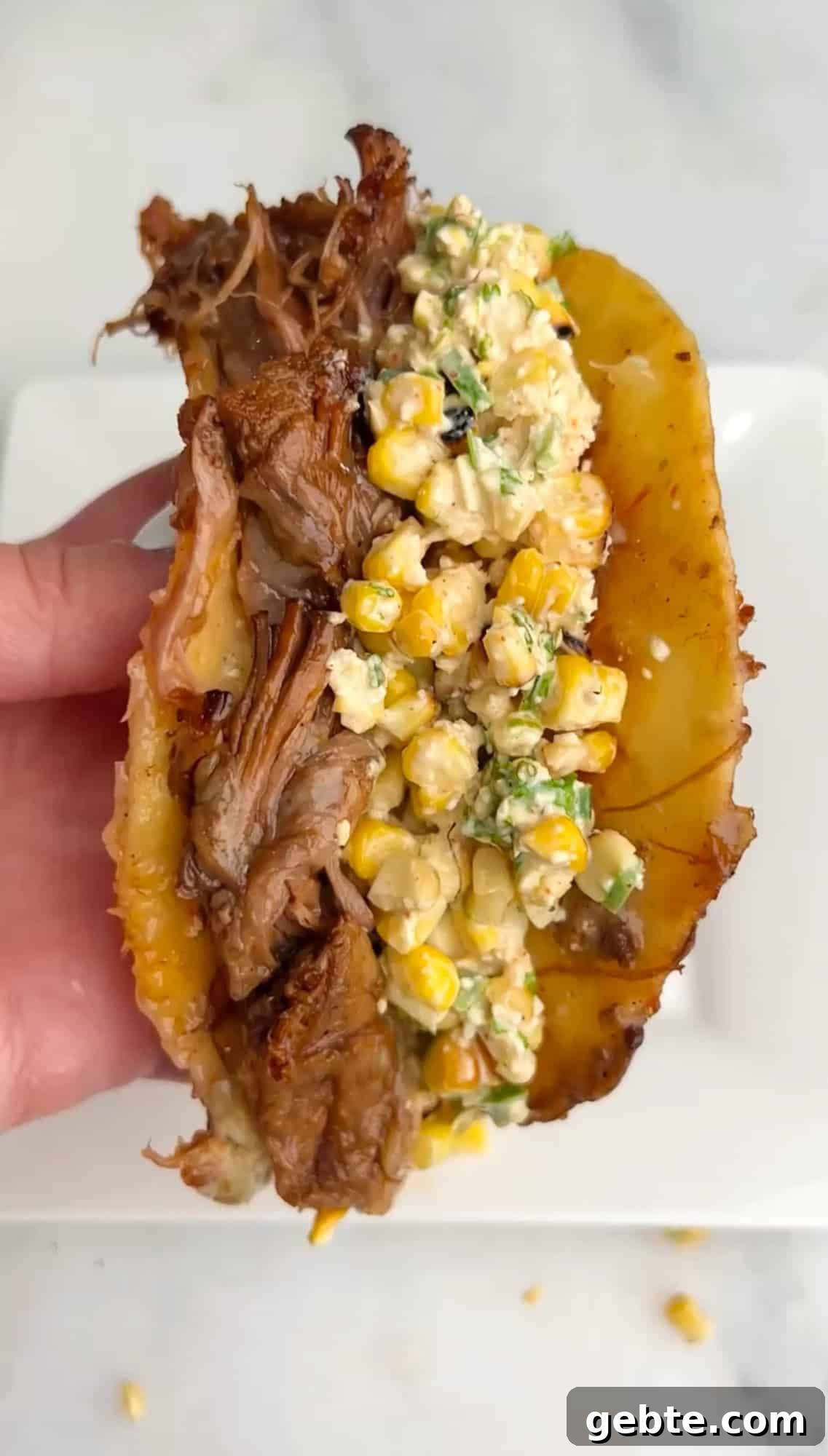 A hand holding a brisket taco with street corn