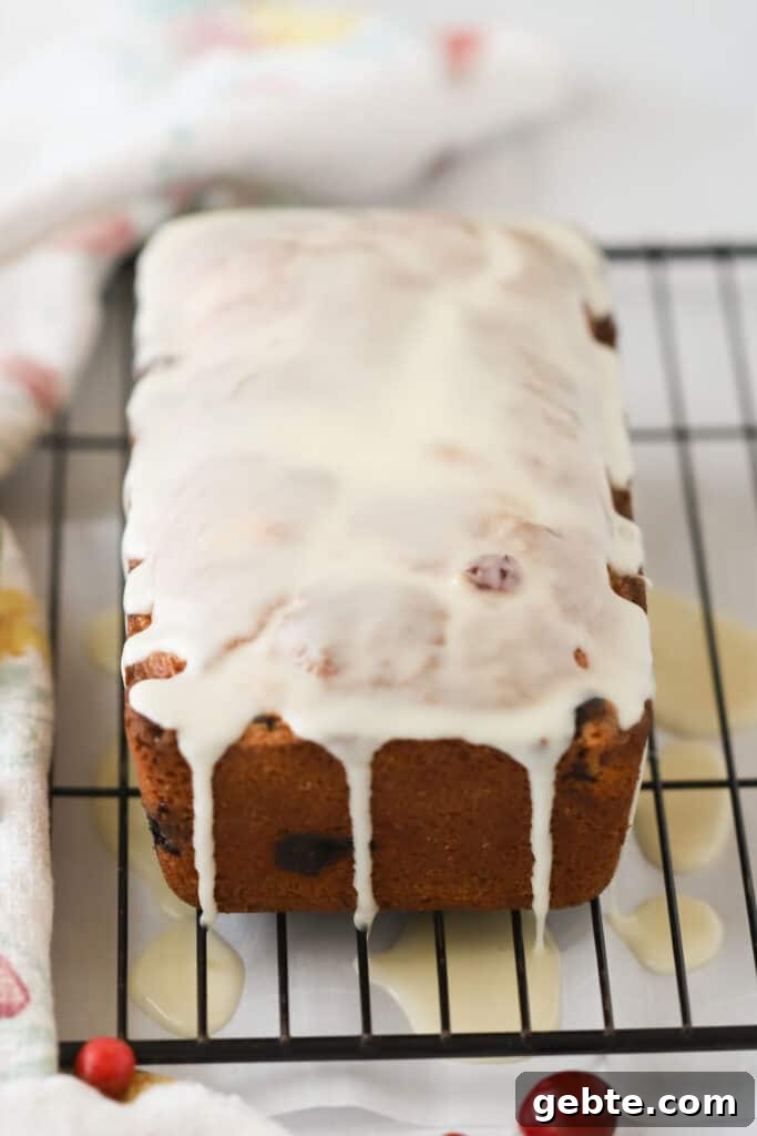 Cranberry Orange Quick Bread Recipe for Holiday Brunch 4 A loaf of cranberry cake recipe on a wire rack with glaze dripping over the top.