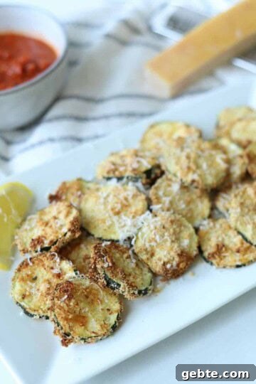 Air fryer zucchini on white plate with lemon wedges and marinara sauce.