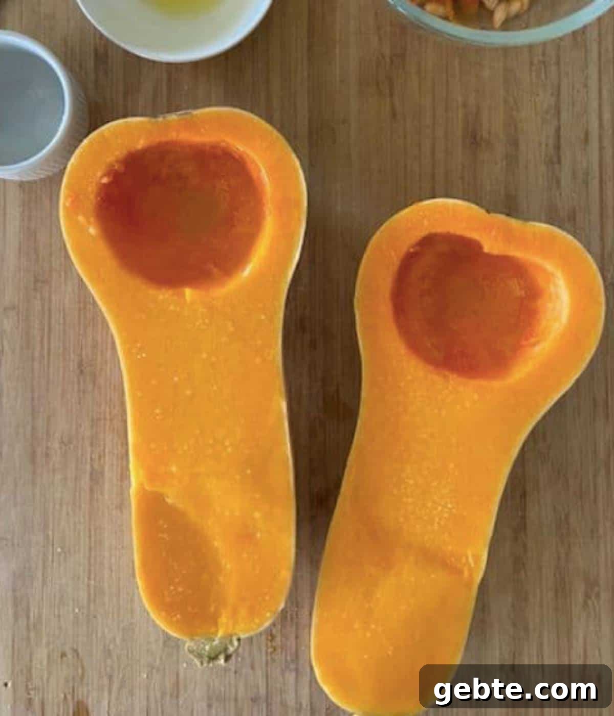 Butternut squash sliced in half with seeds removed on cutting board.