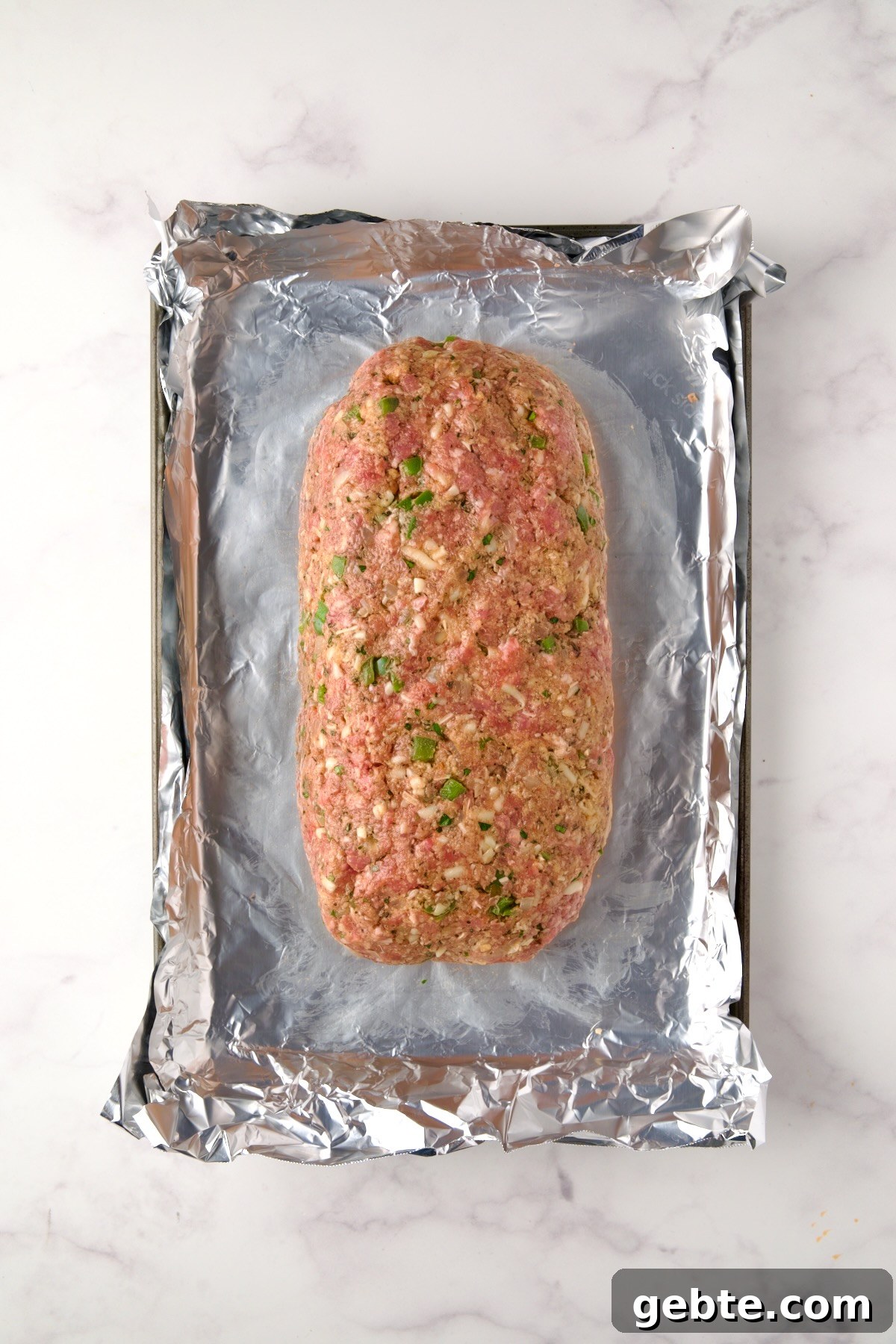 Meatloaf before being baked on aluminum foil-lined rimmed sheet pan.