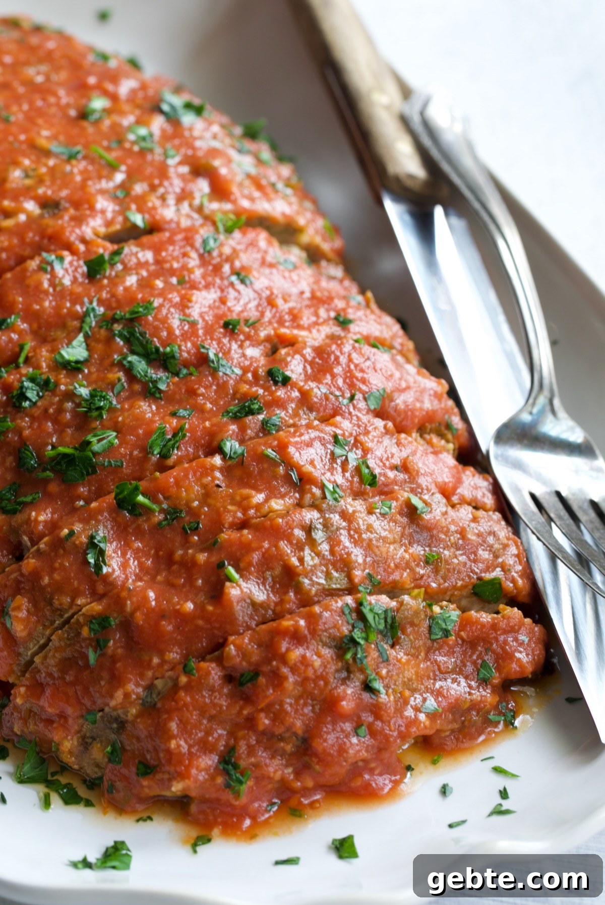 Italian Meatloaf on white platter garnished with chopped fresh parsley.