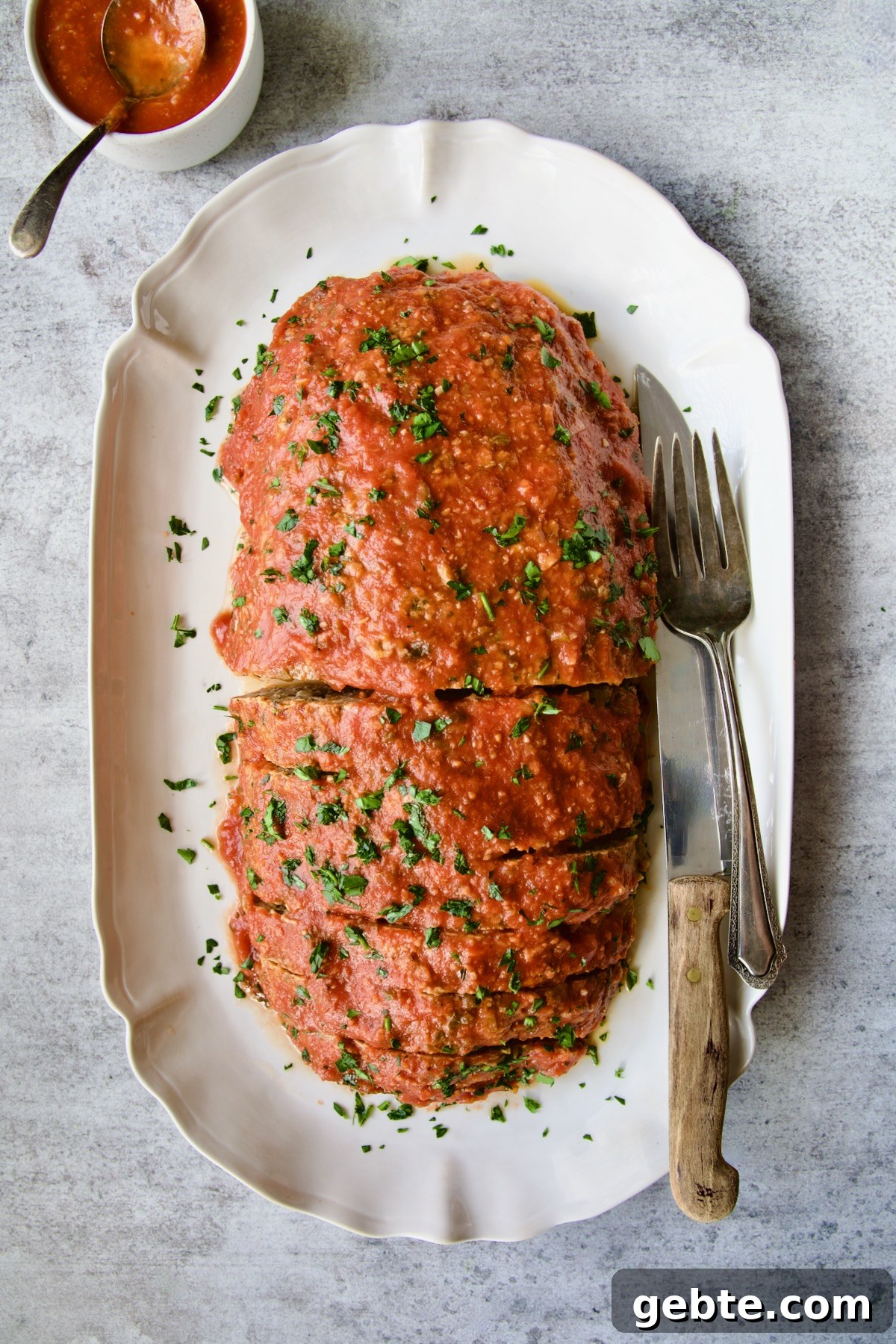 Italian Meatloaf on white platter with serving utensils garnished with chopped fresh parsley.