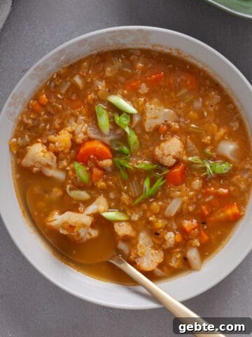A bowl of cauliflower and lentil soup topped with scallions on a gray table.
